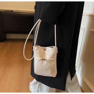 Détail de la mini sacoche en toile crème minimaliste avec cordon de serrage sur manteau noir
