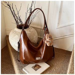 Detail of a brown vintage PU leather hobo bag with plush bear charm and metal tag