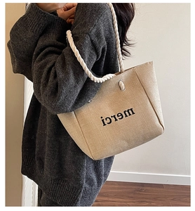 Linen tote bag with merci print and white cotton rope handles shown on shoulder
