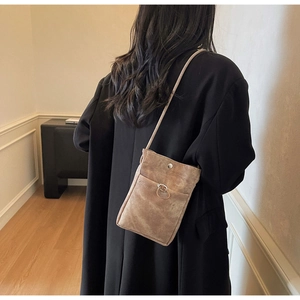 Vue arrière du modèle portant un petit sac bandoulière marron en daim avec un anneau en métal