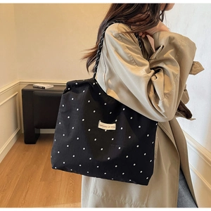 Detail of black floral canvas tote bag with a white label shown on a khaki trench coat