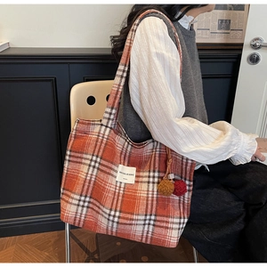 Detail of a large plaid tote bag with colorful pom-pom charms shown on a seated model