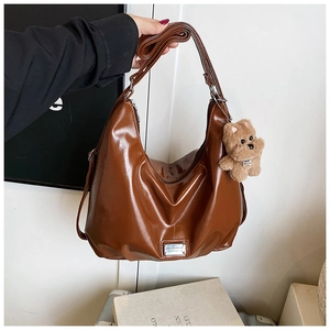 Detail of glossy brown crescent tote bag featuring a cute plush puppy charm and strap