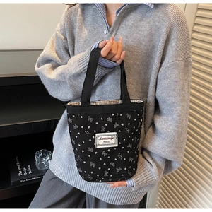 Close-up of black corduroy tote bag with white heart and bow prints held by a model