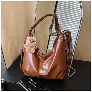 Close-up of brown faux leather tote bag with glossy finish and cute teddy bear pendant