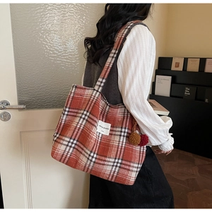 Detail of red plaid tote bag with fuzzy texture, brand label and plush pompom charm
