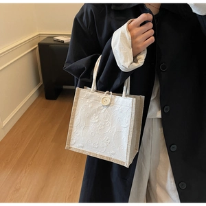 Detail of floral lace embroidery and woven rope handle on an aesthetic linen tote bag
