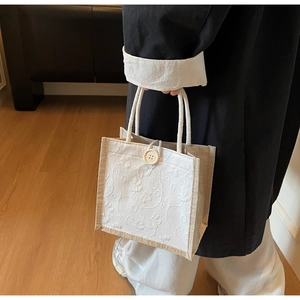 Detail of white embroidered linen tote bag with natural wooden button closure and rope handles