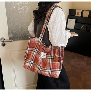 Detail of red orange plaid tote bag with fuzzy pompom charm and logo patch detail