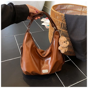Detail of coffee brown glossy leather hobo bag featuring a cute teddy bear charm
