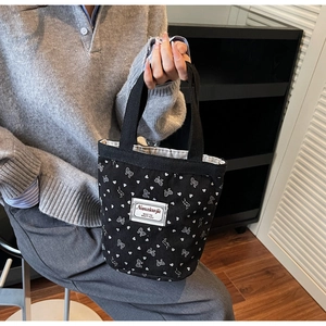 Close-up of black corduroy tote bag with white bow patterns and branded woven label