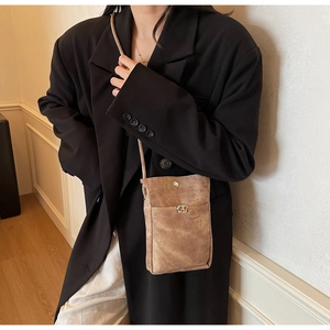 Détail d'un petit sac de téléphone en daim marron porté sur un blazer noir surdimensionné