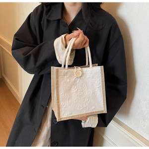 Detail of floral embroidery on a linen tote bag with cream rope handle and button closure