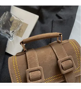 Detail einer braunen Lederhandtasche mit goldener Wellenstickerei und Zierschnallen