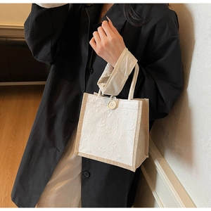 Detailed close-up of a linen hand bag with white floral embroidery and a wooden button closure
