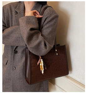 Detail of dark brown leopard embossed tote bag with colorful beaded charm on handle