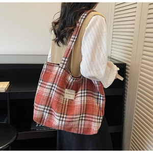 Detailed side view of a large red plaid tote bag made of textured tweed on a model