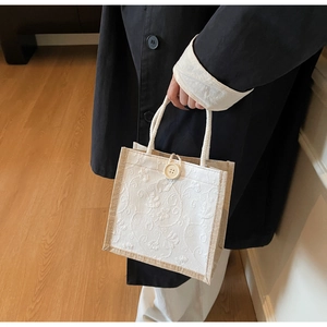 Detail of floral embroidery and woven rope handles on a natural linen lunch tote bag