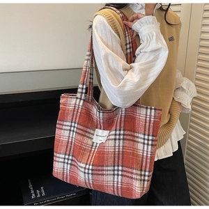 Detail of large canvas tote bag in orange and black plaid with woven brand label