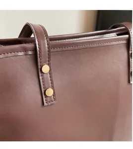 Detailed shot of dark brown leather tote with golden rivets and precise stitching