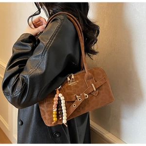 Detailed side view of a brown suede shoulder bag with bohemian beaded charm and metal accents