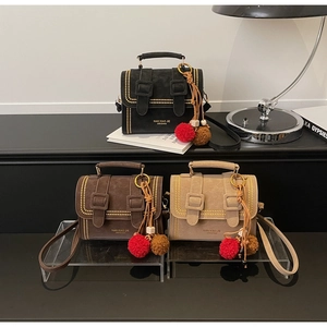 Detail von drei Cambridge-Taschen mit Goldnieten, Branding und Plüsch-Pompon-Anhänger