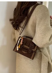 Close-up of dark brown suede handbag featuring gold rivets and colorful beaded charm