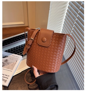 Macro detail of brown woven bucket bag with smooth leather strap and gold metallic buckle