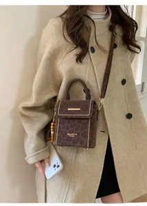Detail of dark brown mini crossbody bag with leopard print and gold rivets on beige coat