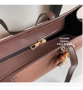 Close-up of brown tote bag showing smooth golden zipper and beaded charm detail