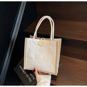 Detail of floral embroidery on cream linen handbag with vintage button and rope handles