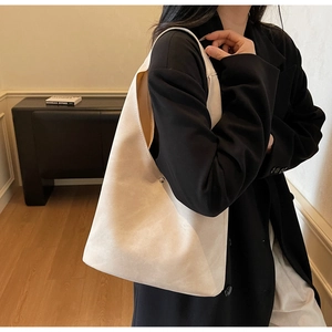 Close-up of a large beige suede shoulder bag with metallic buckle detail on a model