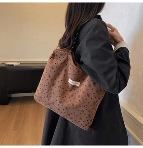 Detailed texture of brown corduroy tote bag with heart and bow patterns on model
