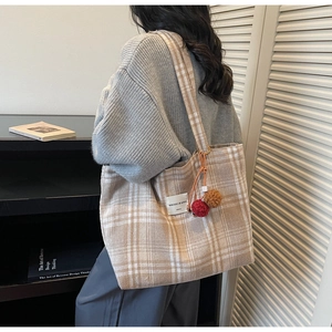 Detail view of large capacity plaid tote bag with plush charm on a female model