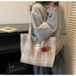 Detail of checkered tote bag with plush pompom charms and minimalist woven texture