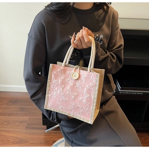Pink tote bag detail with white butterfly embroidery and braided brown side accents