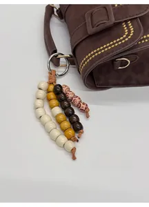 Detail of four-color beaded pendant with wood texture on dark brown handbag
