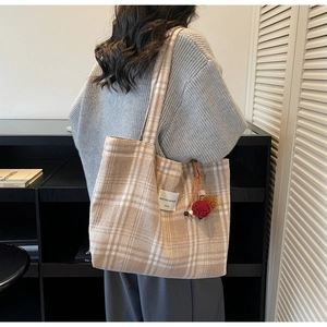 Detail of a large cream plaid tote bag with cozy knitted texture and tassel charm