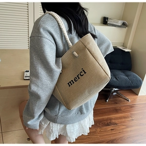 Linen tote bag with black merci print and woven cotton rope handles shown on shoulder