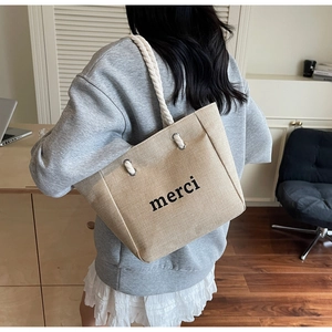 Detail of large linen tote bag with rope handles and merci print on model shoulder