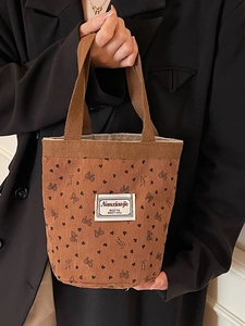 Brown corduroy tote bag with heart and bow patterns shown in a professional handheld view