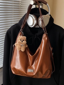 Brown PU leather tote bag with bear charm on hoodie and silver headphones backdrop