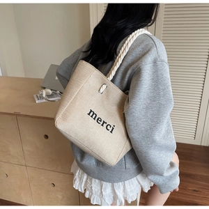 Detail of linen tote bag featuring black merci print and white thick rope handles