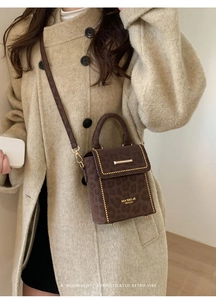 Detail of leopard print handbag with gold rivets and metallic bar closure on suede texture
