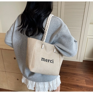 Detail of linen tote bag with 'merci' print, rope handles and metal eyelet reinforcement