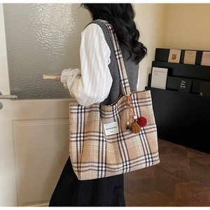 Detail of plaid tote bag with plush pompom charm and logo patch on model side view