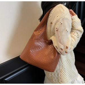 Detail of caramel brown woven leather texture on a trapezoid tote bag with metallic snap