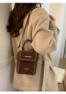 Detail of brown leopard print crossbody bag with gold rivets and metallic logo bar