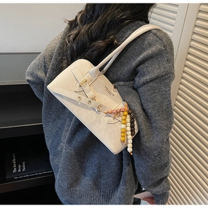 Close-up of minimalist cream leather underarm bag with decorative colorful beads