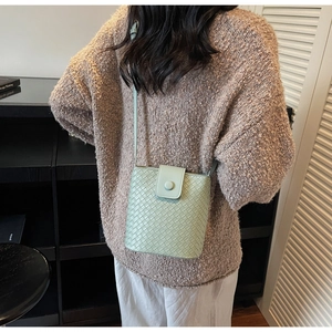 Detail of light green woven crossbody bag with circular snap and slender leather strap